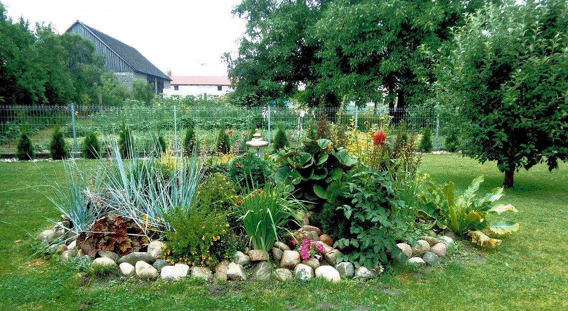 Obraz wiejskiego ogrodu z zabudowaniami w tle.