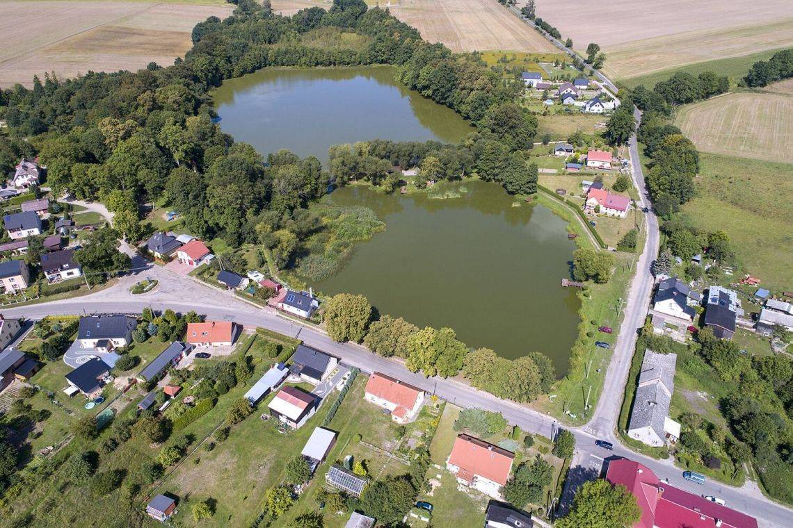 Obraz z lotu ptaka na wieś Redkowice i okolice. Widoczne domy, zagrody, drogi pola, ogrody i dwa stawy.
