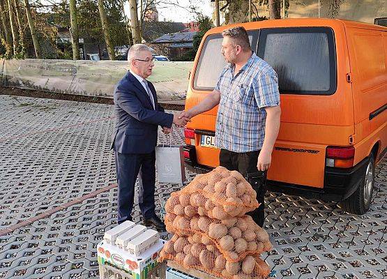 Wójt wręcza mężczyźnie (rolnikowi) torebkę z upominkiem w miejscu sprzedaży.